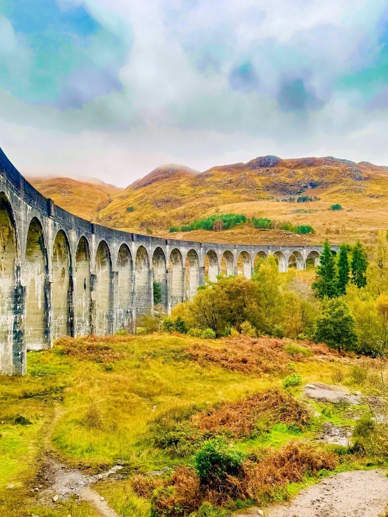 Stone railway viaduct with multiple arches spanning green valley with brown hills and mountains in background