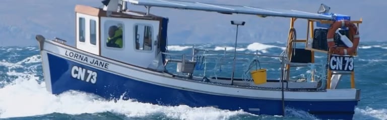 Blue and white fishing boat with registration CV 79 navigating rough ocean waves