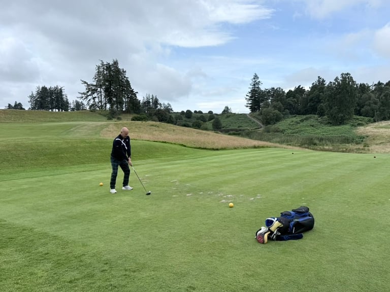 Golfer on lush green fairway with golf bag on ground, rolling hills and trees in background