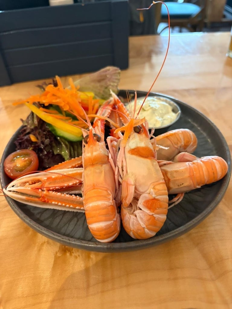 Plated seafood display with lobster tails, shrimp, and vegetables on a black plate with sauce on the side