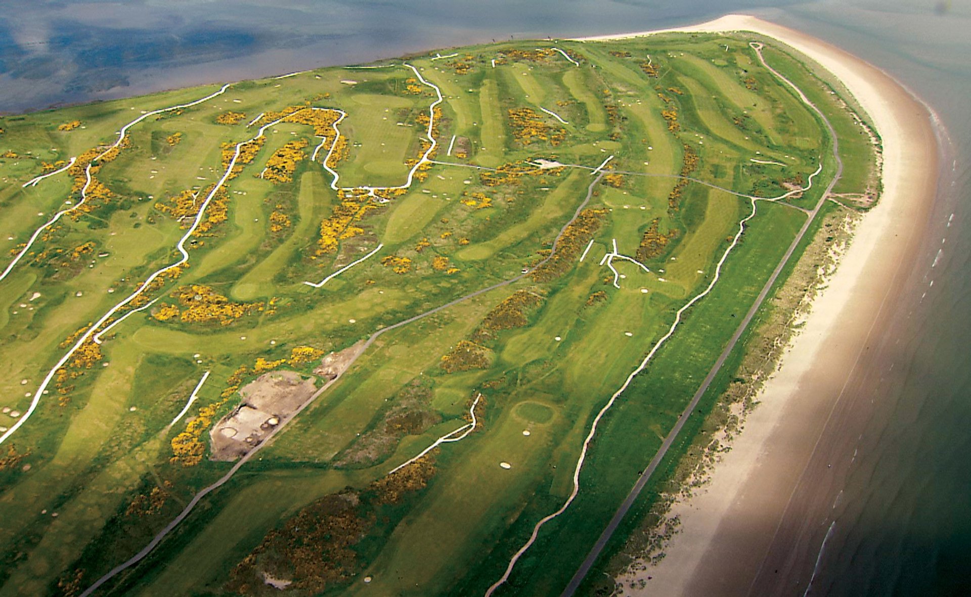 Aerial view of a coastal wetland with winding waterways, green marshland, and sandy beach along the shoreline