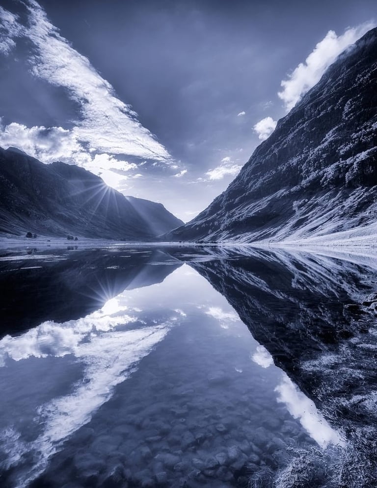Snow-covered mountain valley with perfectly mirrored frozen lake reflecting dramatic sky and peaks
