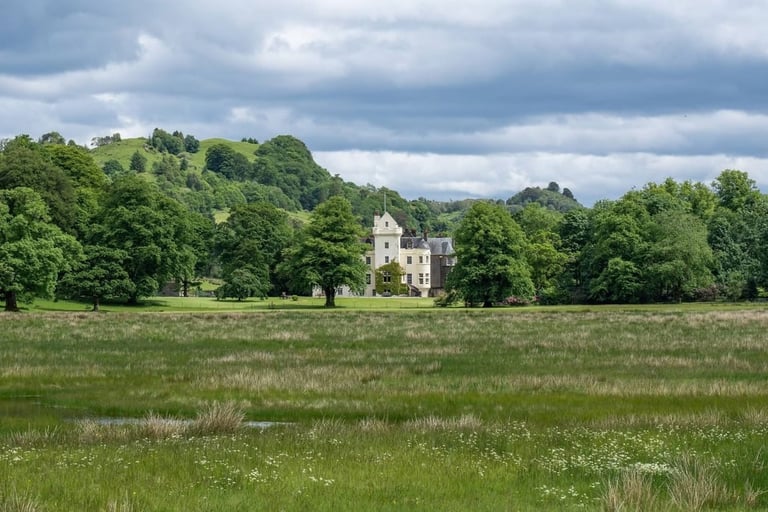 Stone castle surrounded by green woodland and meadow on an overcast day