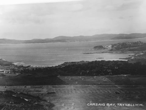 Black and white photograph of Carnsaig Bay, Tayvallich showing a coastal landscape with bay, forested shoreline, and distant hills