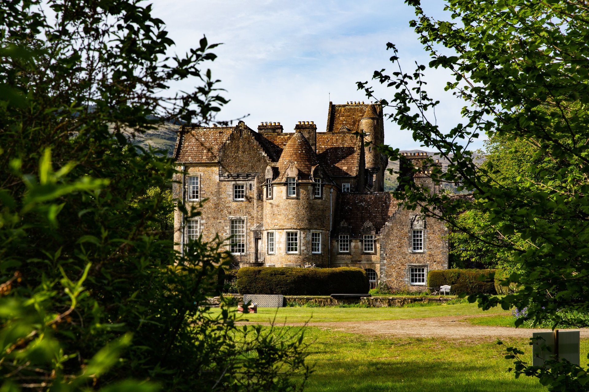 Historic stone castle with towers surrounded by green trees and manicured lawn on a sunny day