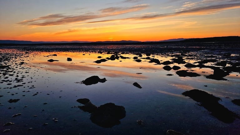 Sunset over a rocky tidal flat with still water reflecting orange and blue sky colors