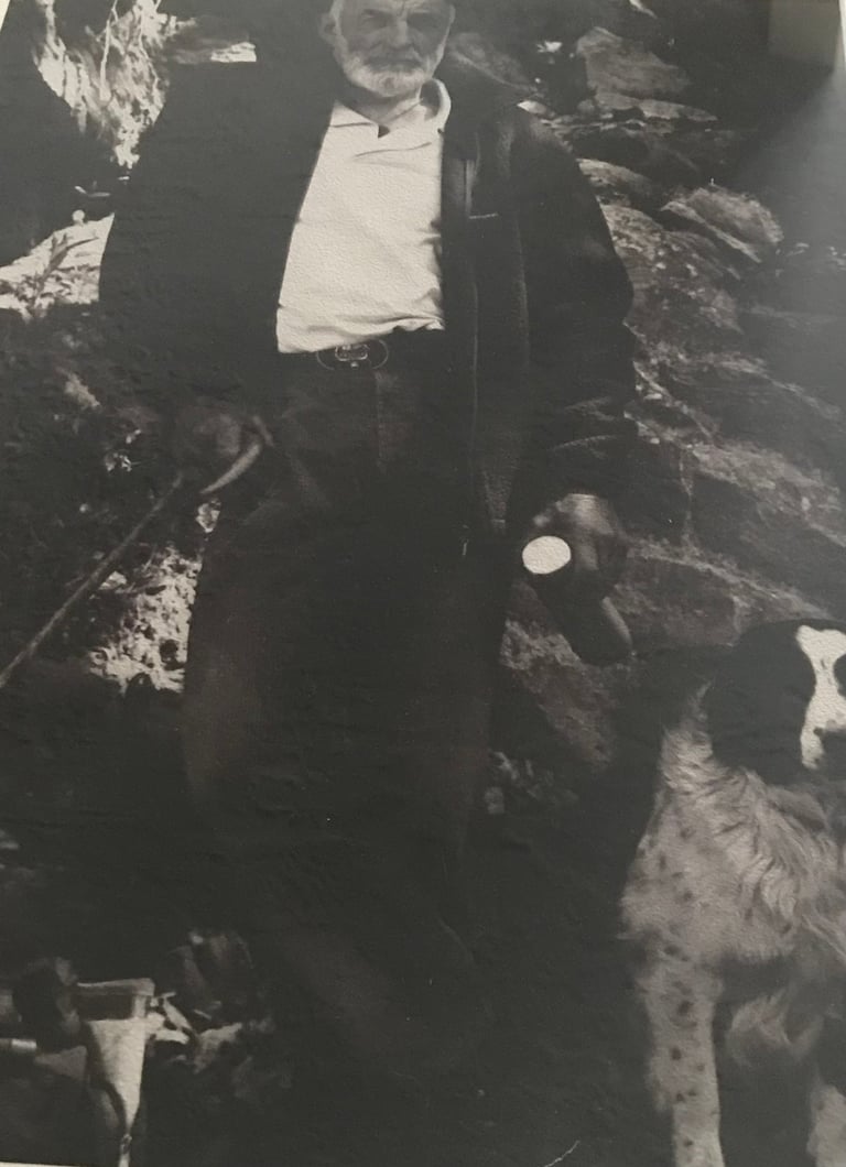 Vintage black and white photo of an older man in formal attire standing among rocky terrain with dogs