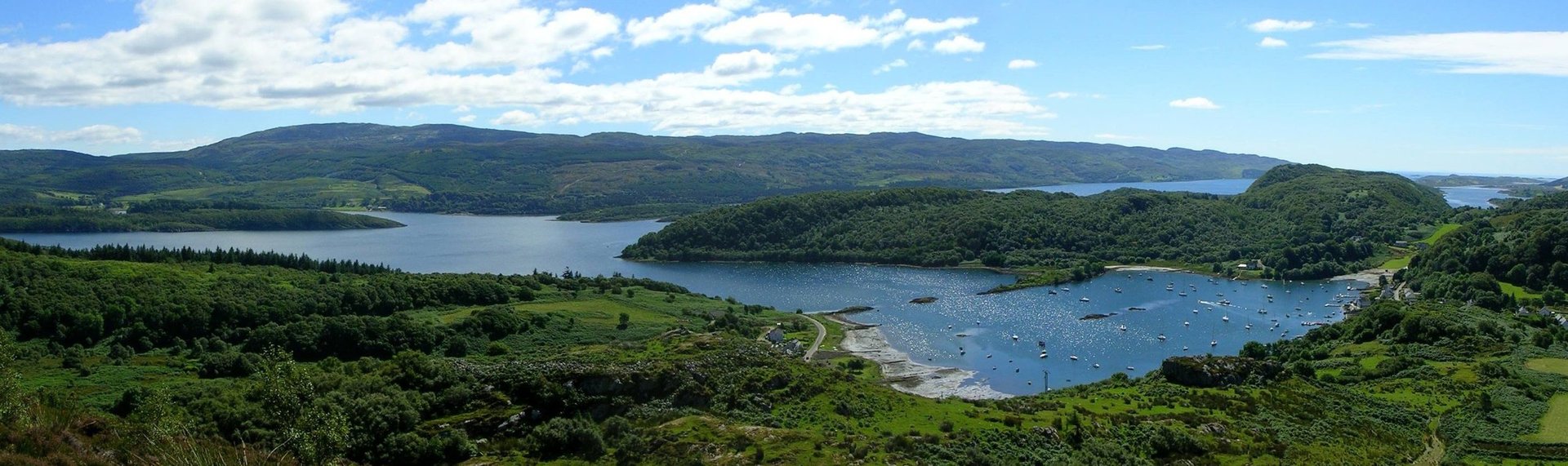 Aerial view of lush green mountains surrounding a blue lake under partly cloudy sky