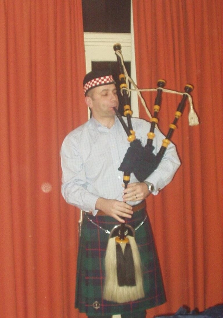 Man in Scottish traditional dress playing bagpipes against red curtain backdrop