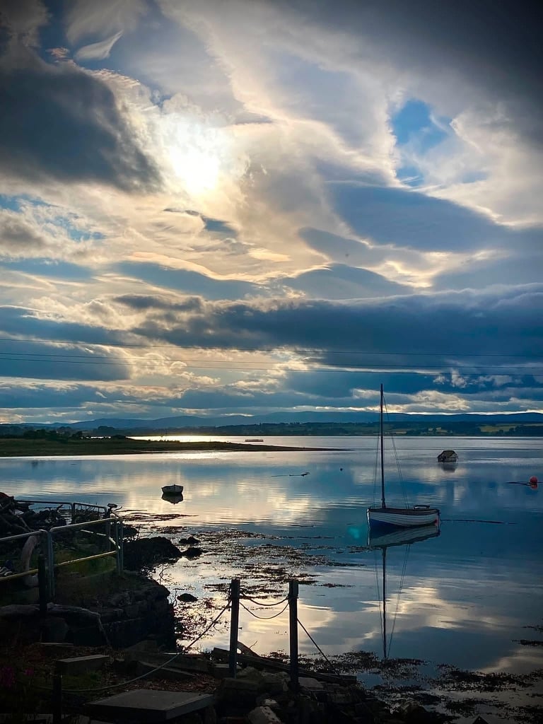 Sailboat moored in calm bay at sunset with dramatic cloudy sky reflected in water