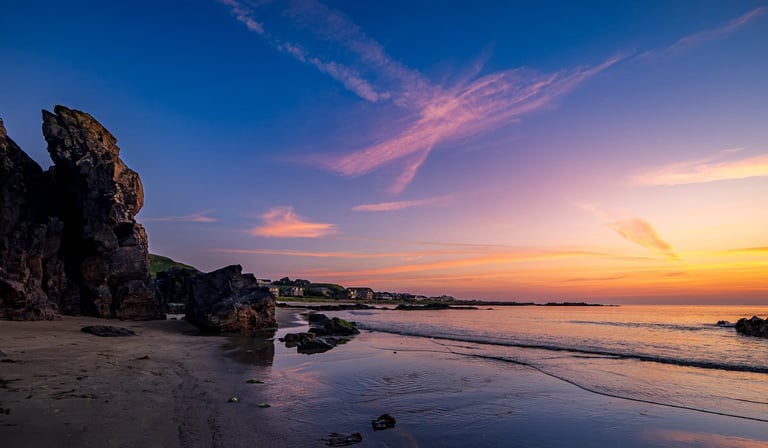 Sunset beach scene with rocky outcrops, calm waves, and vibrant pink and orange sky at dusk