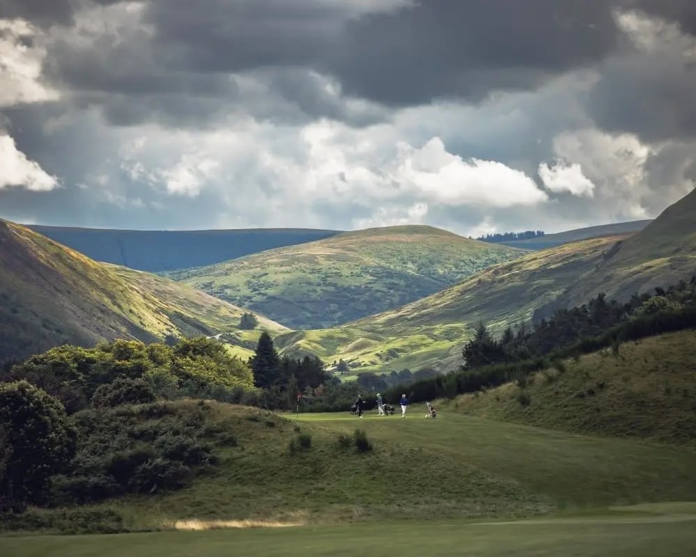 Scenic green valley with rolling hills, scattered trees, and dramatic cloudy sky